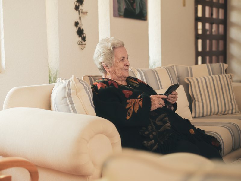 An older woman sitting on her sofa at home, reading something on her phone